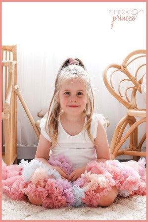 Girl sitting weaing dusty pink soft pastel rainbow ruffles